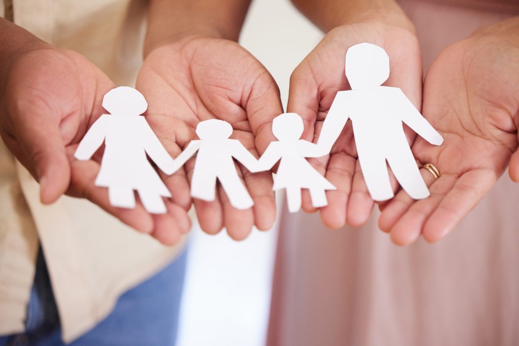 Closeup of a couples hands holding paper cutout of a perfect family. Symbol of home cover, insuranc